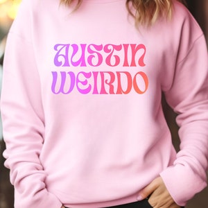 May include: A pink sweatshirt with the text "Austin Weirdo" in a rainbow gradient font.