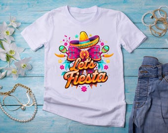 May include: White t-shirt featuring a colorful "Let's Fiesta" design. The graphic includes a sombrero, maracas, and floral elements. The text is in a vibrant orange and yellow gradient, perfect for a festive occasion.