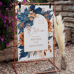 Puede incluir: Un cartel de bienvenida de boda con un diseño floral en tonos azules, naranja y dorado. El cartel dice "Bienvenido a la boda de Helene y Jonathan" con la fecha "09.23.20XX" y las iniciales "H & J".