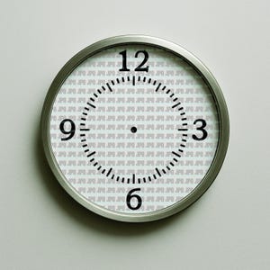 May include: A round, silver-framed wall clock with black numerals at the 12, 3, 6, and 9 o'clock positions. The clock face has a repeating pattern of the text ".JPO". The hands are black and the background is white.