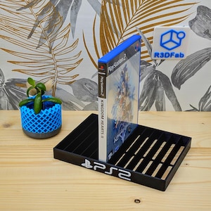 May include: Black plastic stand for a PlayStation 2 video game case. The stand has a slot for the game case and the PlayStation 2 logo on the front. The game case is for Kingdom Hearts II for the PlayStation 2.