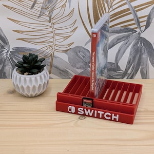 May include: A red plastic storage stand for Nintendo Switch game cases and cartridges. The front features the white Nintendo Switch logo and text. One game case for The Legend of Zelda: Tears of the Kingdom and one game cartridge are inserted.