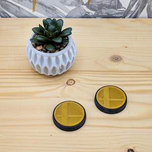 May include: Two round, black and gold coasters with a stylised "Smash" logo. The coasters are on a light wood surface.
