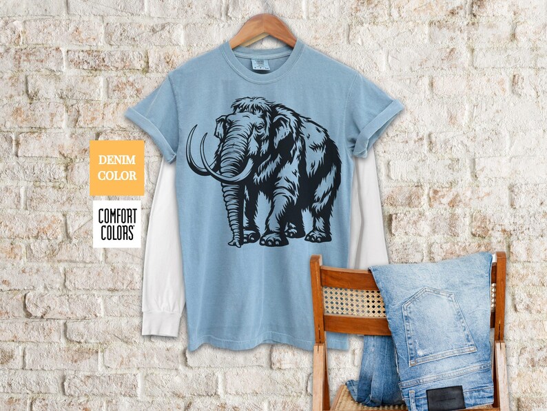 May include: A light blue t-shirt with a black and white illustration of a woolly mammoth. The shirt has a white underlay and is made of a soft, comfortable fabric.