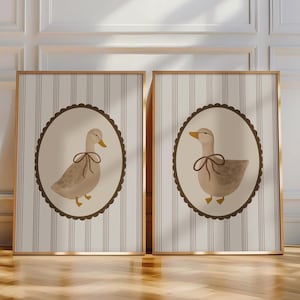 May include: Two framed prints with a striped background and a brown oval frame. Each frame features a watercolor illustration of a duck with a brown bow tie.