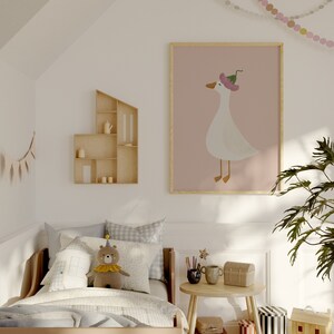 May include: A light wood bed with a white and blue checkered duvet and a stuffed bear wearing a party hat. A framed print of a white goose wearing a pink hat is on the wall above the bed. A small wooden shelf with a teapot and cups is on the wall to the left of the bed. A small round table with a wooden top and legs is in the corner of the room. There is a wooden toy house and a black and white striped toy box on the floor.