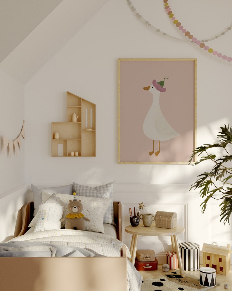 May include: A light wood bed with a white and blue checkered duvet and a stuffed bear wearing a party hat. A framed print of a white goose wearing a pink hat is on the wall above the bed. A small wooden shelf with a teapot and cups is on the wall to the left of the bed. A small round table with a wooden top and legs is in the corner of the room. There is a wooden toy house and a black and white striped toy box on the floor.