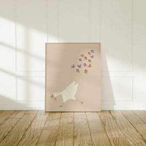 May include: A white goose with a pink beak runs to the right, chasing a flock of purple and orange butterflies on a light pink background.