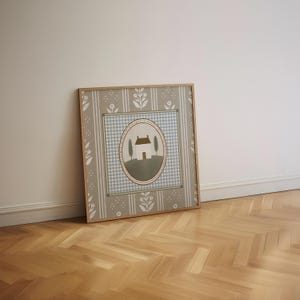 May include: A framed print with a light blue and white gingham pattern, a green and white house, and two green trees. The print is surrounded by a brown frame and has a beige background with white floral patterns.