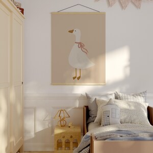 May include: A children's bedroom scene featuring a large wall art print of a white goose with a pink bow. The room includes a wooden bed, a nightstand with a lamp, and a plush goose toy on the floor. Pastel colors dominate the decor.