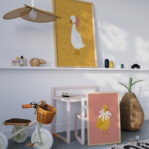 Pu&ograve; includere: Un'illustrazione di un'oca bianca e gialla con un fiocco rosa su uno sfondo giallo con puntini rosa. Una seconda illustrazione di un'oca gialla con un colletto di fiori bianchi su uno sfondo rosa. Entrambe le illustrazioni sono incorniciate in legno.