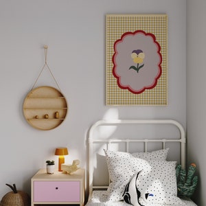 May include: A white metal bed frame with a white and black polka dot duvet cover and a black and white polka dot pillow. A green cactus plush toy is on the bed. A framed print with a yellow flower on a pink and red background is hanging on the wall.