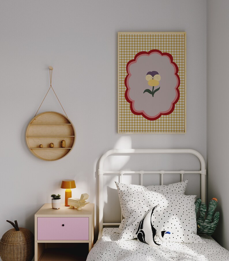May include: A white metal bed frame with a white and black polka dot duvet cover and a black and white polka dot pillow. A green cactus plush toy is on the bed. A framed print with a yellow flower on a pink and red background is hanging on the wall.