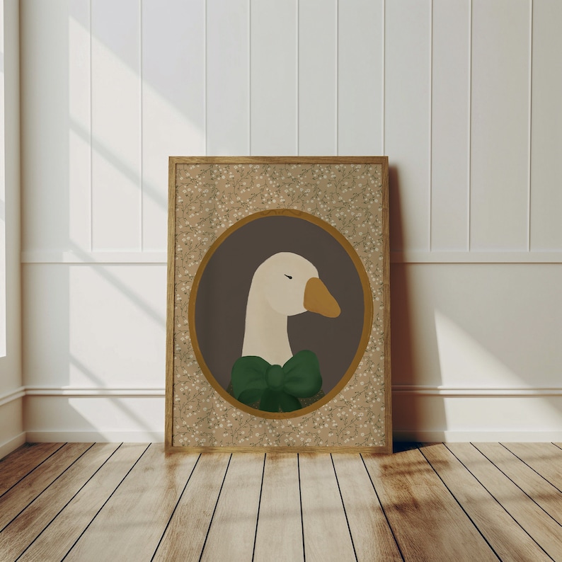 May include: A framed print of a white goose wearing a green bow tie. The goose is in a circular frame with a brown background and a floral pattern border.
