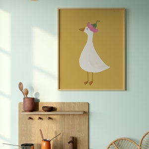 May include: A framed illustration of a white goose wearing a pink flower on its head. The goose is standing on a yellow background.