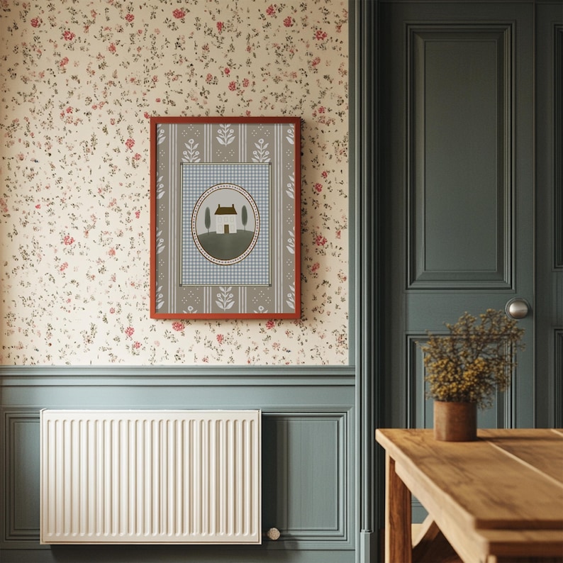 May include: A framed print with a blue and white checkered background and a small house illustration in the center. The frame is red with a brown mat. The print is hanging on a wall with a floral wallpaper.