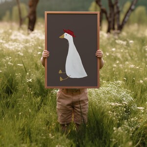 May include: A child holds up a framed illustration of a white goose wearing a red hat. The goose is sitting with its legs crossed and has a gold beak.