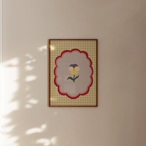 May include: A framed print with a yellow, purple, and green flower on a light gray background. The frame has a yellow and red gingham pattern.