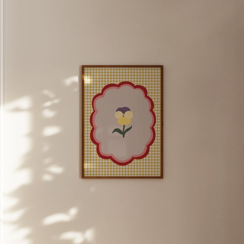 May include: A framed print with a yellow, purple, and green flower on a light gray background. The frame has a yellow and red gingham pattern.