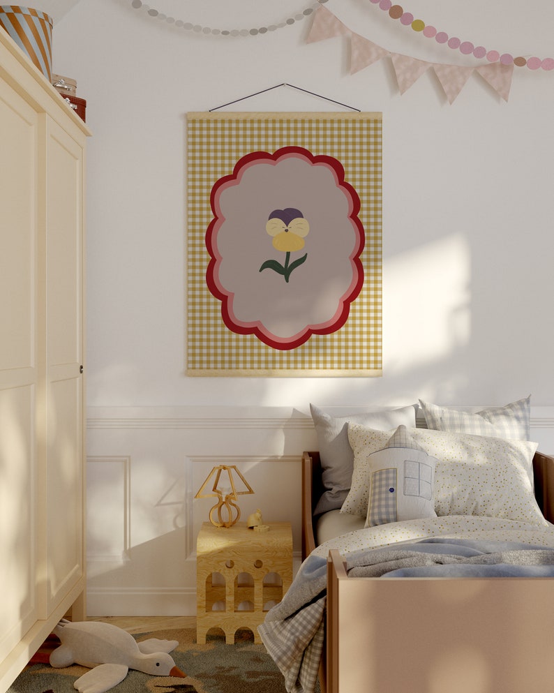 May include: A yellow, red, and purple flower with a green stem is printed on a beige and brown gingham fabric poster. The poster is hanging on a white wall in a bedroom with a bed, a nightstand, and a lamp.