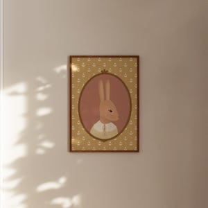 May include: A framed illustration of a brown rabbit wearing a white sweater and a pink bow. The rabbit is in an oval frame with a pink background. The frame is surrounded by a yellow pattern of small flowers.
