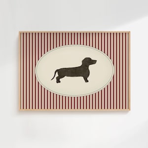 May include: A framed print featuring a dachshund illustration. The dog is depicted in a dark color against a cream-colored oval. The background has vertical red and white stripes. The frame is a light brown color.