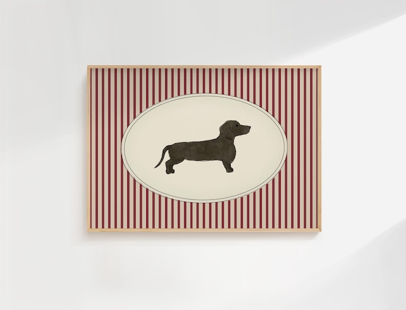 May include: A framed print featuring a dachshund illustration. The dog is depicted in a dark color against a cream-colored oval. The background has vertical red and white stripes. The frame is a light brown color.