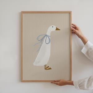 Könnte beinhalten: Eine gerahmte Illustration einer weißen Gans mit einer blauen Schleife auf einem beige gestreiften Hintergrund.