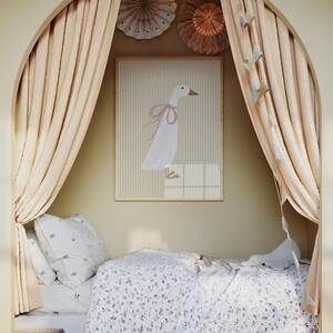 May include: A white bed with a white and brown floral patterned duvet cover and a white pillow with a small floral pattern. The bed is in a nook with beige curtains and a white framed print of a pink-ribboned goose. The print is on a beige wall with paper decorations.