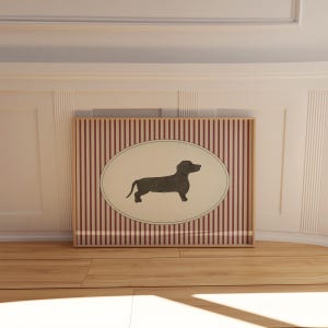 May include: A framed artwork featuring a dachshund silhouette within an oval. The background has vertical red and white stripes. The artwork is displayed on a wooden floor.