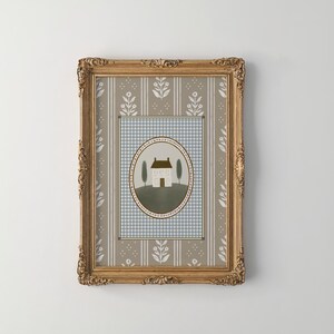 May include: A framed print of a house with a brown roof and white walls, surrounded by two green trees. The house is set against a blue and white checkered background with a floral pattern border. The frame is gold with ornate details.