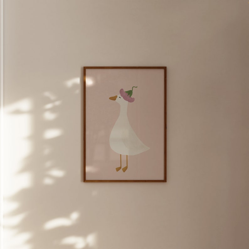 May include: A framed print of a white goose wearing a pink flower on its head. The goose is facing right and has a light pink background.