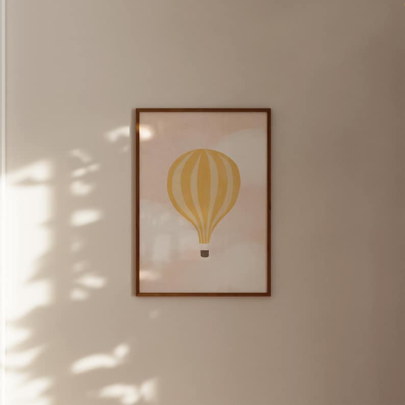 May include: A framed print of a yellow hot air balloon with white stripes against a light pink background.