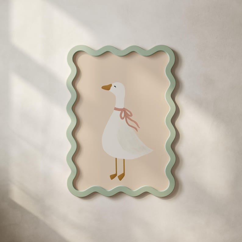May include: A framed wall art print featuring a white goose with a pink ribbon around its neck. The goose is set against a light peach background, framed by a wavy, light green border. The artwork is mounted on a white wall.
