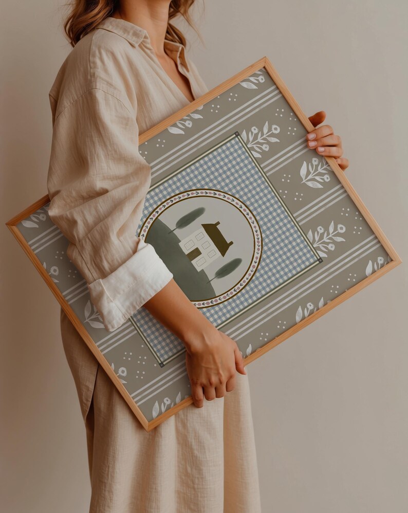 May include: A framed print with a light blue and white gingham pattern, a white house with green trees, and a floral border on a gray background.