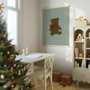 May include: A white wooden desk with a chair and a Christmas tree in the corner. A framed print of a brown teddy bear on a green and white gingham background hangs on the wall.