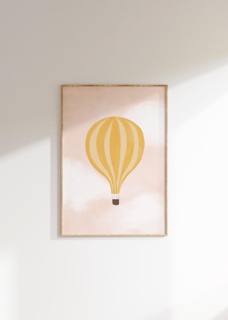 May include: A framed print of a yellow hot air balloon with white stripes floating in a pink sky with white clouds.