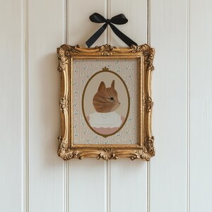 Pode incluir: Uma impress&atilde;o emoldurada de um gato usando um colar rosa e uma camisa branca, com um fundo de padr&atilde;o floral.