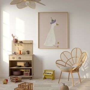 May include: A light wood play kitchen with a toy stove, shelves, and a toy truck. A wicker chair with a light brown cushion sits in front of a pink framed print of a white goose wearing a purple flower on its head. A yellow toy piano sits on the floor.