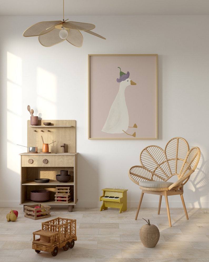 May include: A light wood play kitchen with a toy stove, shelves, and a toy truck. A wicker chair with a light brown cushion sits in front of a pink framed print of a white goose wearing a purple flower on its head. A yellow toy piano sits on the floor.