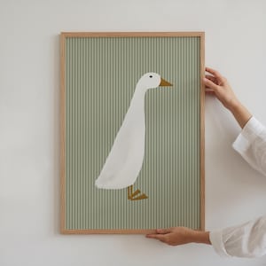 May include: A framed print of a white goose with a yellow beak and feet on a green striped background.