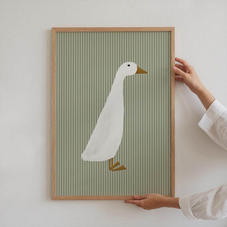 May include: A framed print of a white goose with a yellow beak and feet on a green striped background.