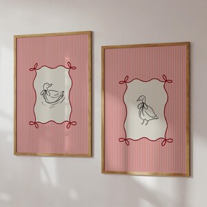 May include: Two framed prints with pink and white striped backgrounds. Each print features a black and white illustration of a duck inside a red, white, and black frame.
