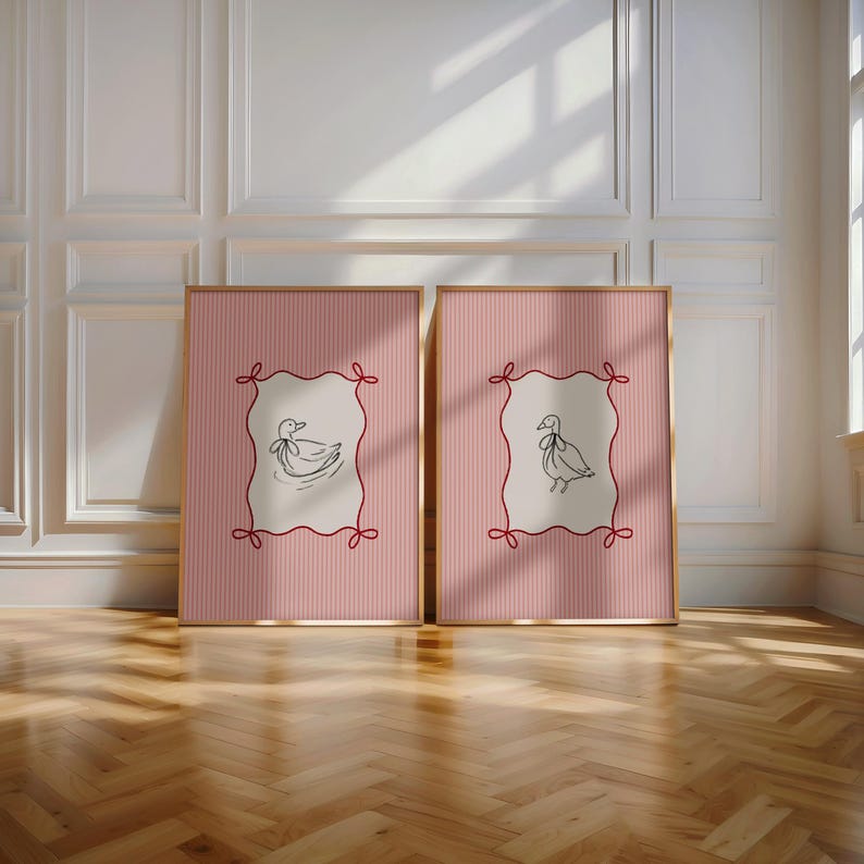 May include: Two framed prints with pink and white striped backgrounds. Each print features a black and white illustration of a duck inside a white frame with red ribbon accents.