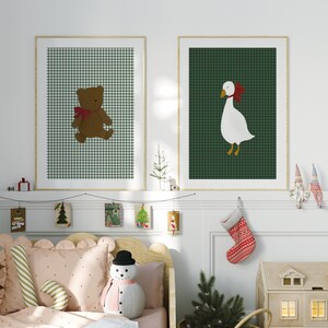 May include: Two framed illustrations of a teddy bear and a goose wearing red bows on a green and white gingham background. The frames are hanging on a white wall above a bed with a pink and white patterned duvet and a snowman plush toy.