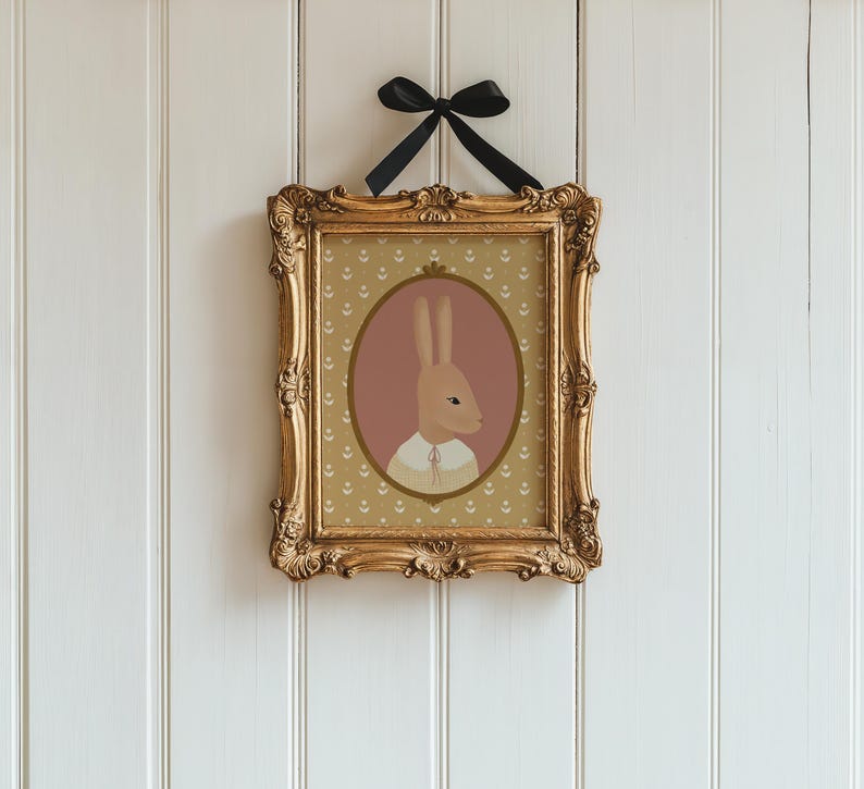 May include: A framed print of a brown rabbit wearing a white shirt with a pink background and a gold frame.