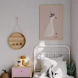May include: A white metal bed frame with a white and black polka dot duvet cover and a white pillow with black polka dots. A white stuffed animal with black eyes and a black and green cactus are on the bed. A framed print of a white goose wearing a purple flower on its head is hanging on the wall.