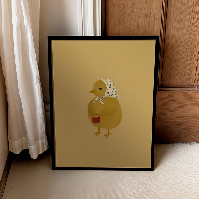 Puede incluir: Una ilustraci&oacute;n enmarcada de un pollito amarillo que lleva un pa&ntilde;uelo estampado en azul y blanco. El pollito sostiene un peque&ntilde;o cubo rojo en su ala derecha. El fondo es de color amarillo claro.