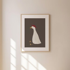 May include: A framed illustration of a white goose wearing a red hat, sitting on a brown background.