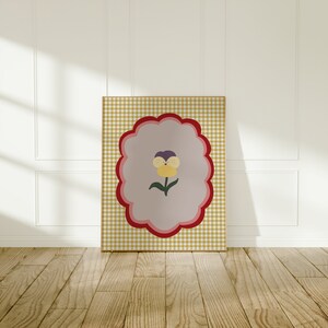 May include: A framed print with a yellow, purple, and green flower on a light pink background. The background is a yellow and white gingham pattern.